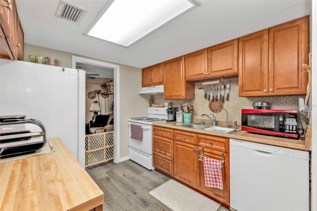 kitchen featuring white appliances, visible vents, light wood-style flooring, under cabinet range hood, and a sink