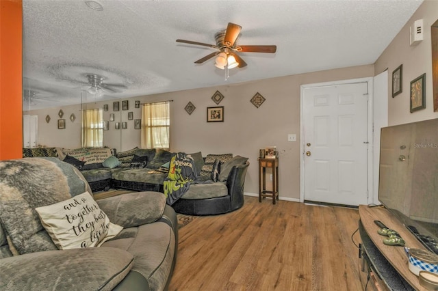 living area featuring baseboards, ceiling fan, a textured ceiling, and light wood finished floors