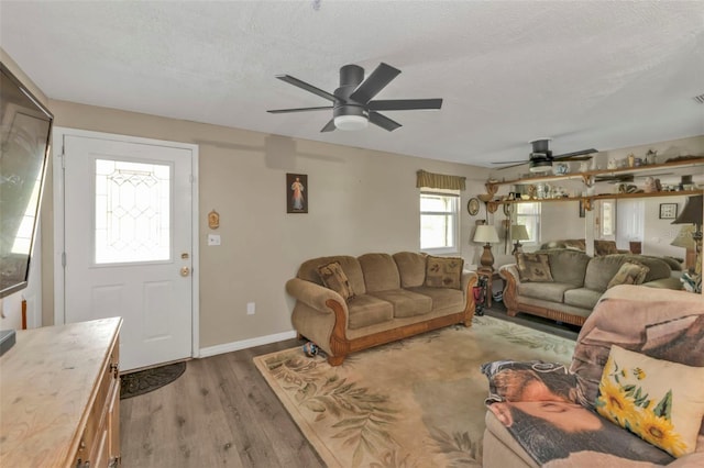 living area featuring light wood-style floors, ceiling fan, baseboards, and a textured ceiling