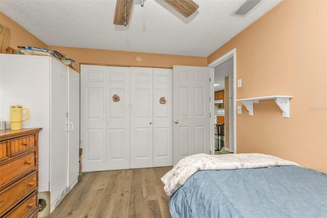 bedroom with a textured ceiling, a ceiling fan, visible vents, light wood-style floors, and a closet