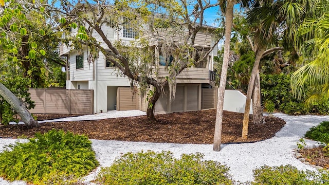 raised beach house featuring fence, driveway, and stucco siding