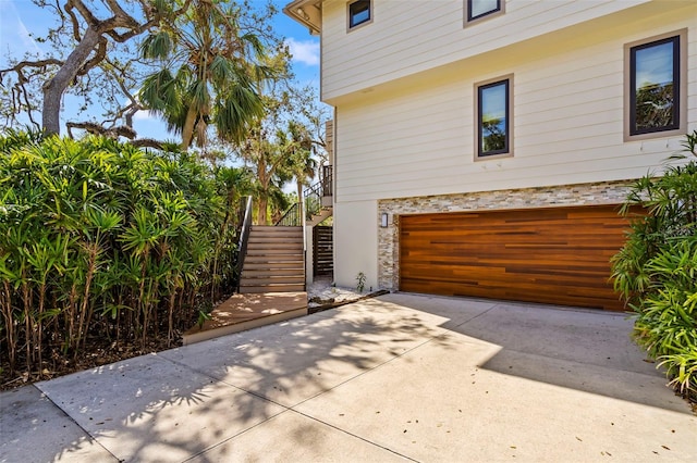 view of property exterior with driveway, an attached garage, and stairway