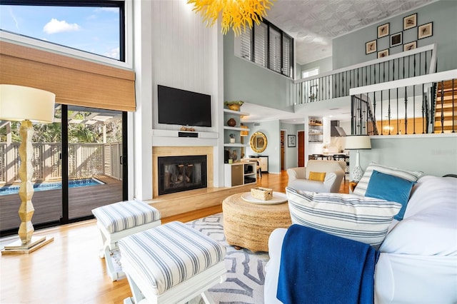 living area featuring stairs, wood finished floors, a glass covered fireplace, and a towering ceiling