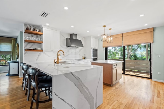 kitchen with tasteful backsplash, a wealth of natural light, a sink, and wall chimney range hood