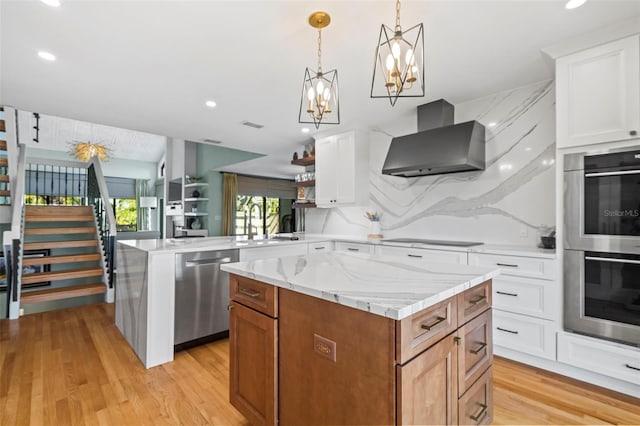 kitchen featuring a peninsula, a sink, a kitchen island, appliances with stainless steel finishes, and wall chimney exhaust hood