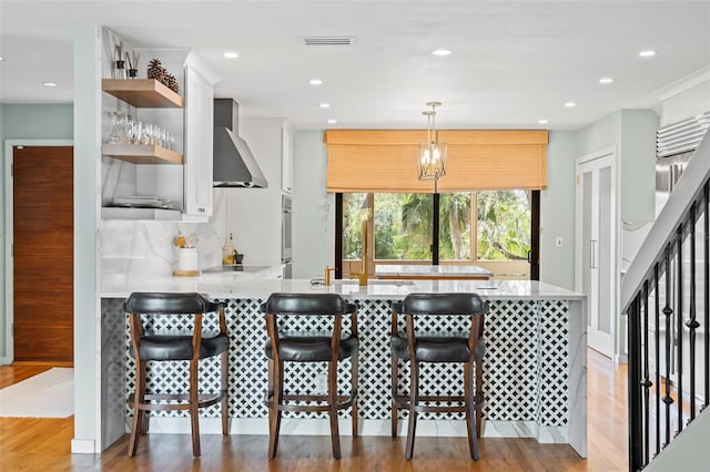 kitchen featuring black electric stovetop, open shelves, visible vents, wall chimney range hood, and a peninsula