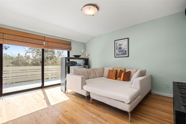 living room featuring lofted ceiling, light wood-style flooring, and baseboards