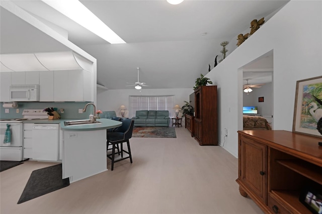 kitchen featuring white cabinets, a sink, white appliances, a peninsula, and a kitchen bar