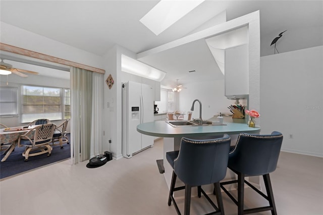 kitchen with white fridge with ice dispenser, ceiling fan, a peninsula, and a kitchen bar