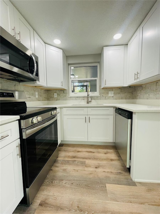 kitchen featuring white cabinets, decorative backsplash, appliances with stainless steel finishes, light countertops, and a sink