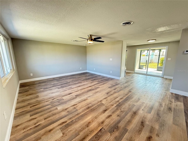 empty room with wood finished floors, visible vents, a textured ceiling, and ceiling fan