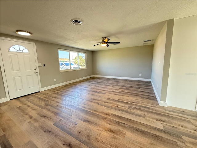 foyer entrance featuring ceiling fan, wood finished floors, a textured ceiling, and visible vents