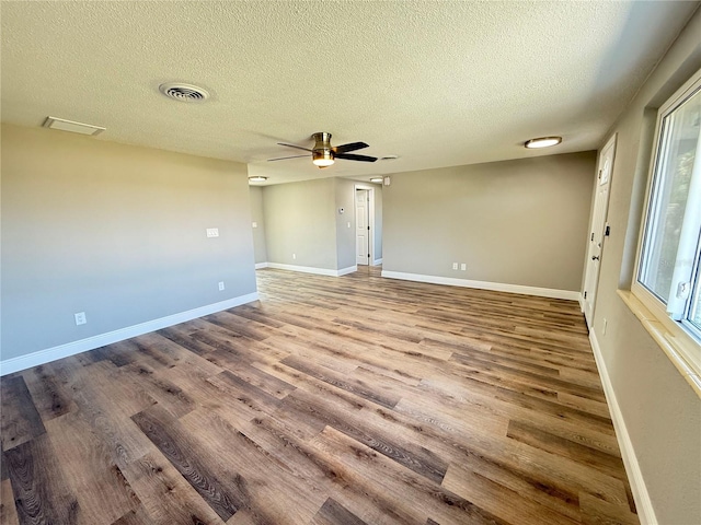 unfurnished room featuring a textured ceiling, visible vents, baseboards, a ceiling fan, and wood finished floors
