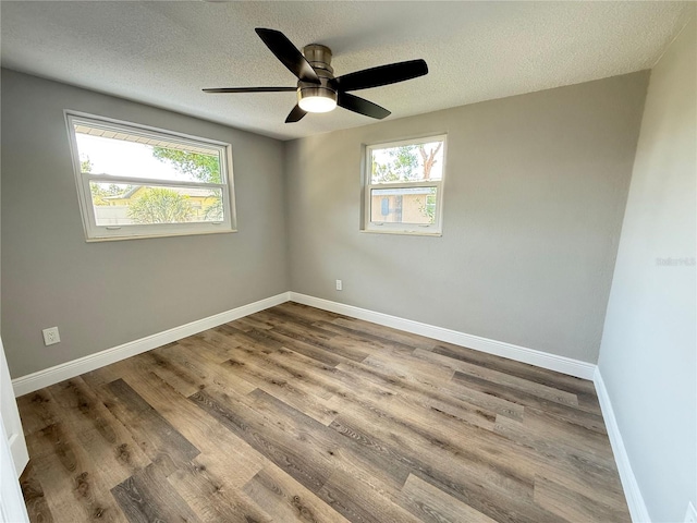 unfurnished room with a textured ceiling, wood finished floors, a wealth of natural light, and a ceiling fan