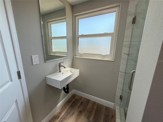 full bath with wood finished floors, a textured wall, a sink, baseboards, and a stall shower