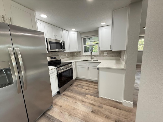 kitchen featuring light countertops, backsplash, a sink, light wood-style flooring, and appliances with stainless steel finishes