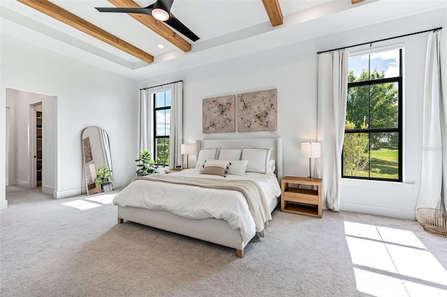 bedroom featuring multiple windows, beamed ceiling, a ceiling fan, and light colored carpet