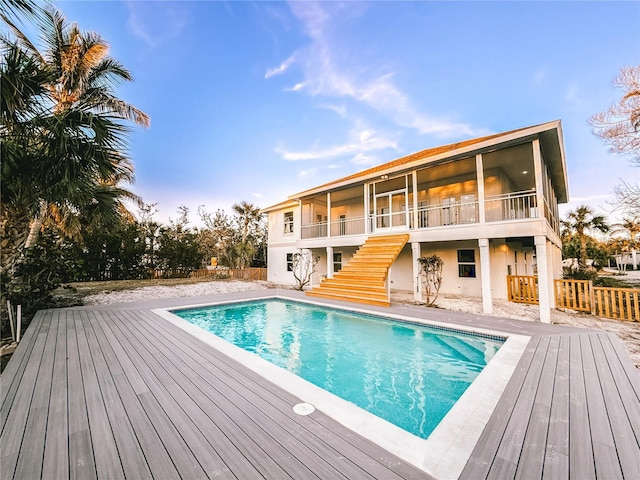 back of house featuring an outdoor pool, stairs, fence, a wooden deck, and stucco siding