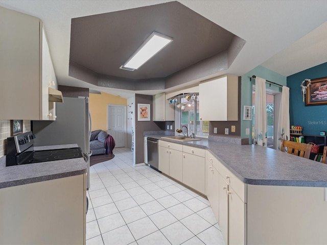 kitchen featuring light tile patterned floors, stainless steel appliances, a peninsula, a sink, and a tray ceiling