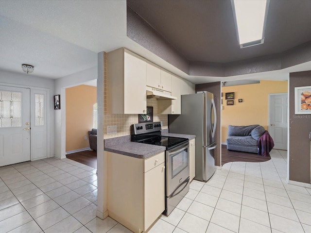 kitchen with under cabinet range hood, backsplash, electric stove, and light tile patterned flooring