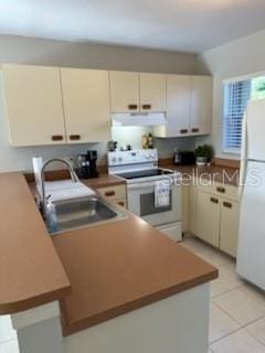 kitchen with cream cabinetry, light tile patterned floors, a sink, white appliances, and under cabinet range hood