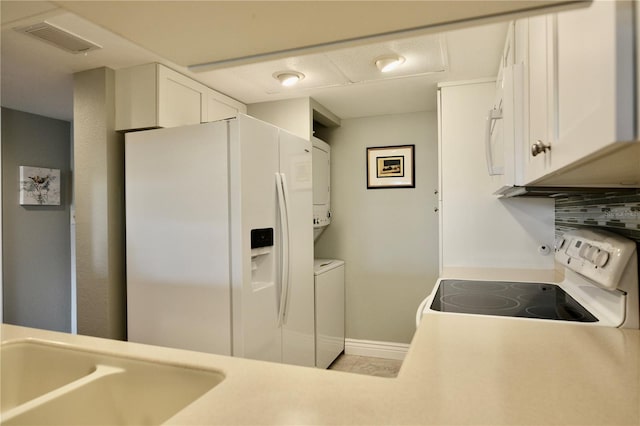 kitchen featuring stacked washer / drying machine, visible vents, decorative backsplash, white cabinets, and white appliances