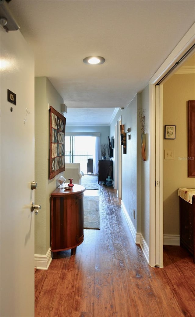 hallway with ornamental molding, wood finished floors, and baseboards