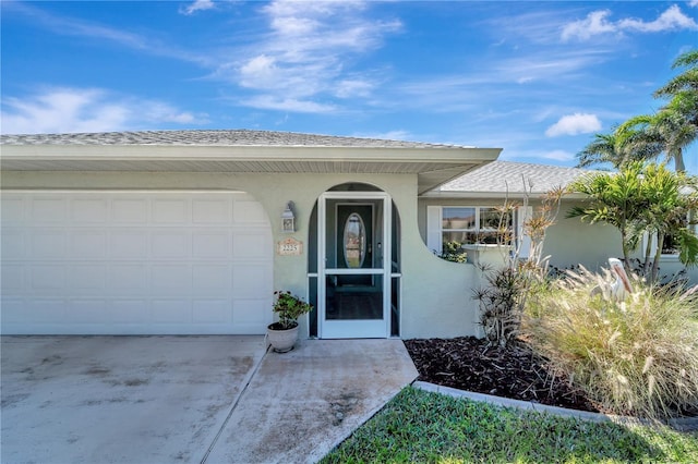 doorway to property featuring stucco siding, a garage, concrete driveway, and a shingled roof