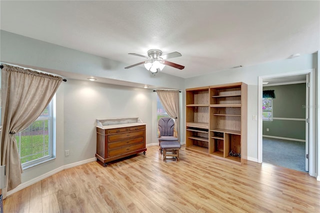 living area featuring baseboards, light wood-style floors, and a ceiling fan