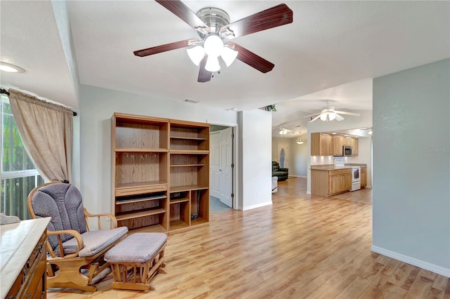 living area with baseboards, vaulted ceiling, light wood-style flooring, a textured ceiling, and a ceiling fan