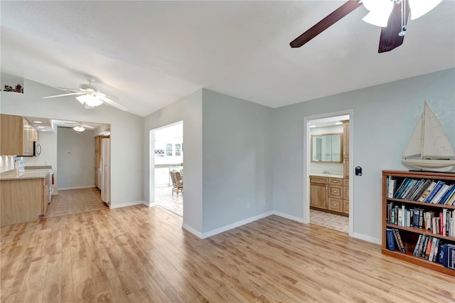 living area with light wood finished floors, baseboards, ceiling fan, and vaulted ceiling