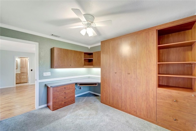 office with a ceiling fan, visible vents, built in desk, light carpet, and crown molding