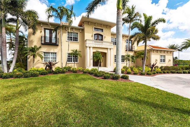 mediterranean / spanish-style house featuring a front yard, a balcony, driveway, and stucco siding