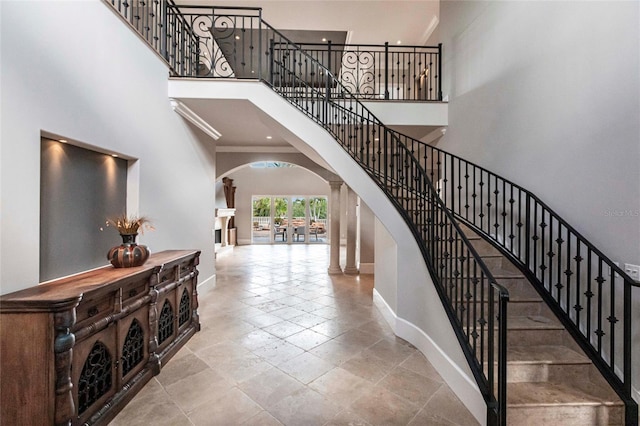 stairway featuring arched walkways, a high ceiling, baseboards, and ornamental molding