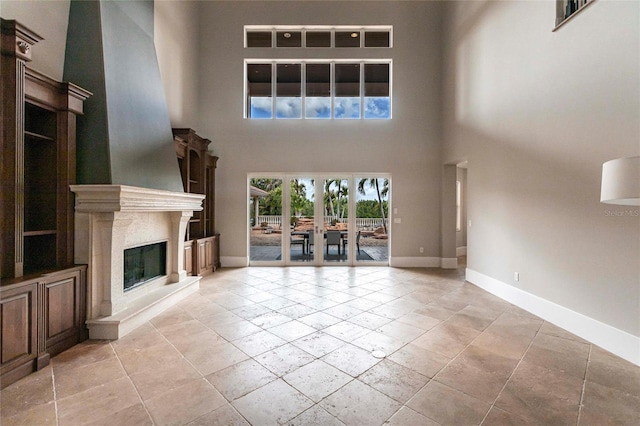 unfurnished living room featuring french doors, baseboards, a high ceiling, and a high end fireplace