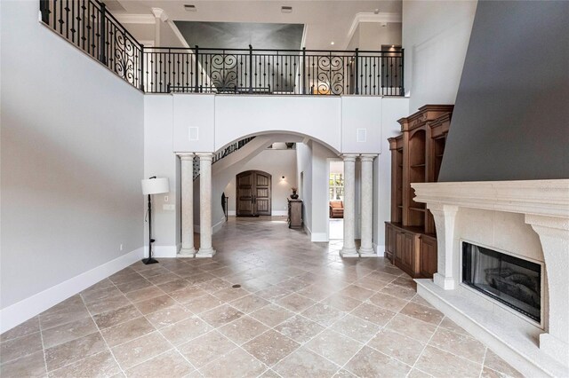 unfurnished living room with a glass covered fireplace, decorative columns, arched walkways, and baseboards