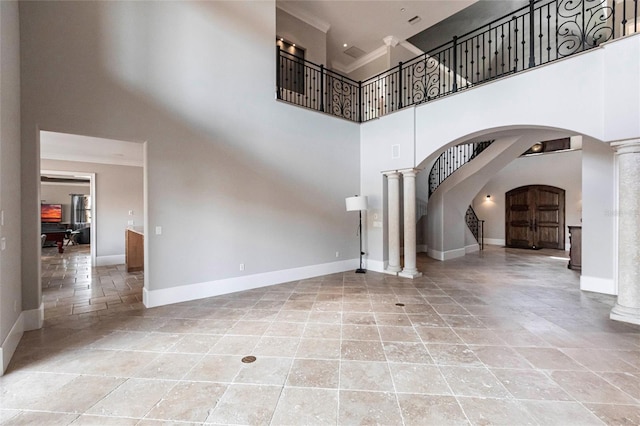 unfurnished living room with ornamental molding, arched walkways, baseboards, stairs, and ornate columns