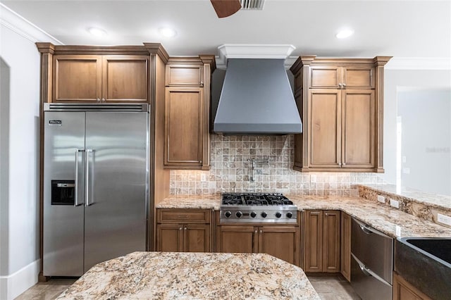 kitchen with light stone counters, premium range hood, stainless steel appliances, decorative backsplash, and crown molding