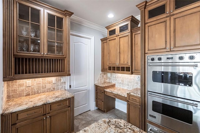 kitchen featuring decorative backsplash, crown molding, light stone countertops, and stainless steel double oven