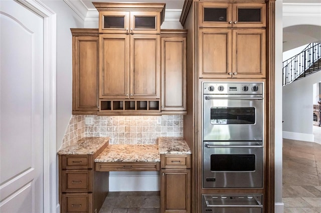 kitchen with backsplash, double oven, ornamental molding, brown cabinetry, and a warming drawer