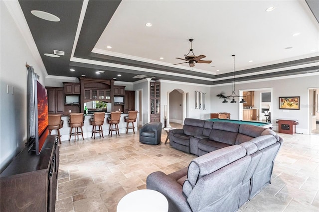 living room with a raised ceiling, arched walkways, a ceiling fan, and stone finish floor