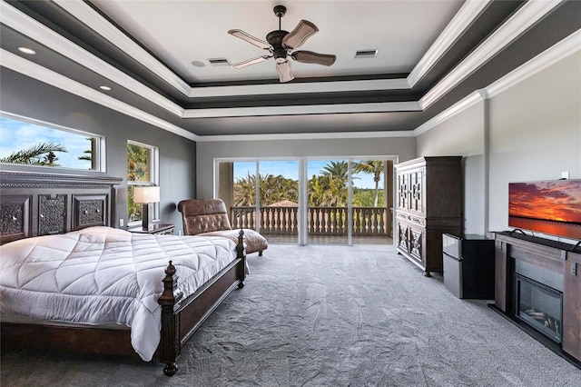 carpeted bedroom with access to exterior, a glass covered fireplace, crown molding, and a tray ceiling