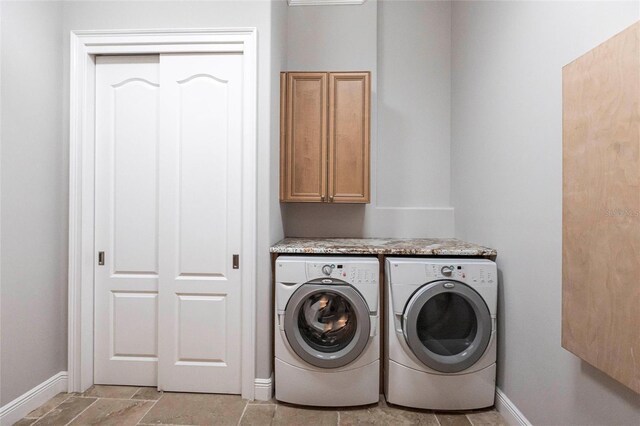 clothes washing area featuring stone finish floor, cabinet space, baseboards, and washing machine and clothes dryer