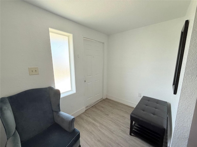 living area with a textured ceiling, light wood-style flooring, and baseboards