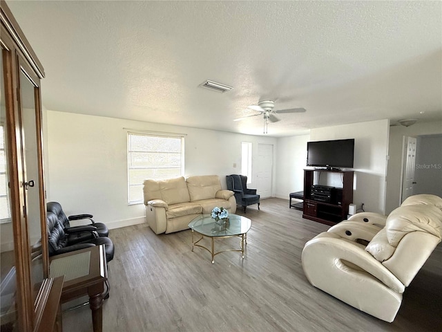 living room featuring a textured ceiling, light wood-style flooring, visible vents, baseboards, and a ceiling fan