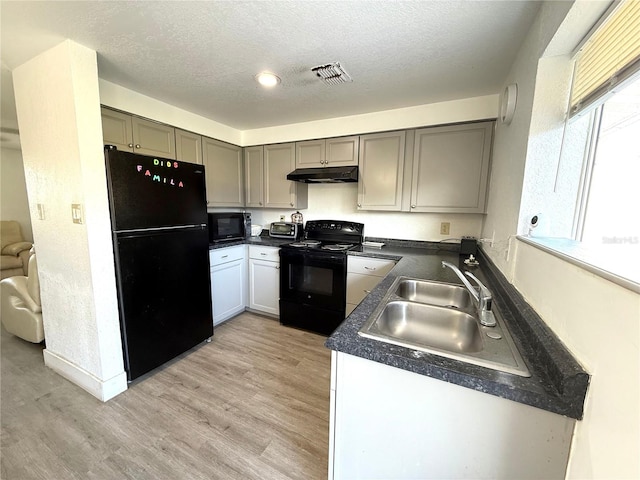 kitchen with under cabinet range hood, a sink, visible vents, black appliances, and dark countertops