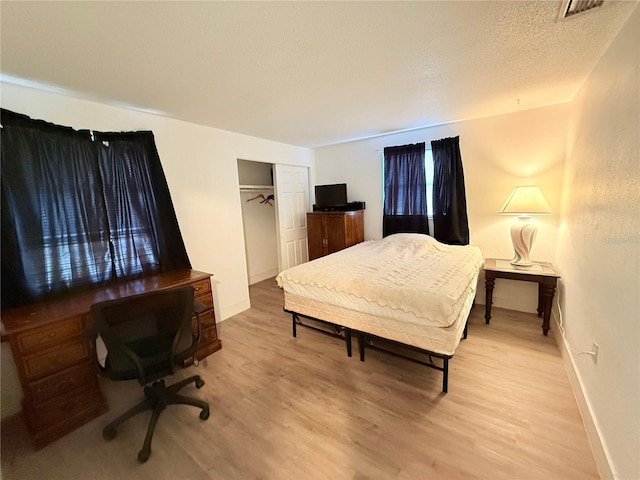 bedroom featuring a closet, visible vents, a textured ceiling, light wood-type flooring, and baseboards