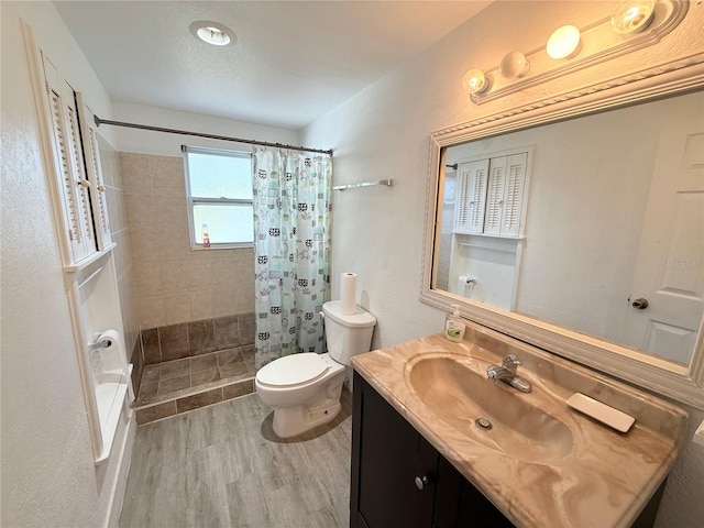 full bath featuring toilet, a tile shower, wood finished floors, and vanity