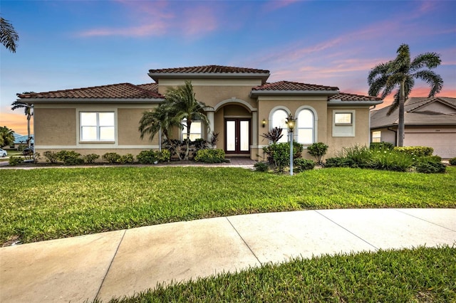 mediterranean / spanish-style house with stucco siding, a tiled roof, a lawn, and french doors