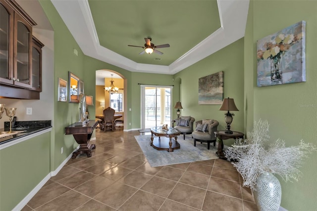 living area with arched walkways, ceiling fan with notable chandelier, dark tile patterned flooring, baseboards, and a tray ceiling